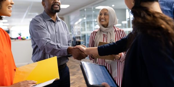 Happy diverse female and male businesspeople talking and shaking hands in office. Business, corporation, cooperation and working in office concept.